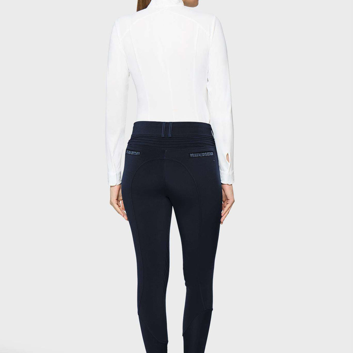 A woman shown from the back wearing a white mock-neck long-sleeve top and dark navy blue skinny pants, paired with white sneakers, against a light gray studio background.