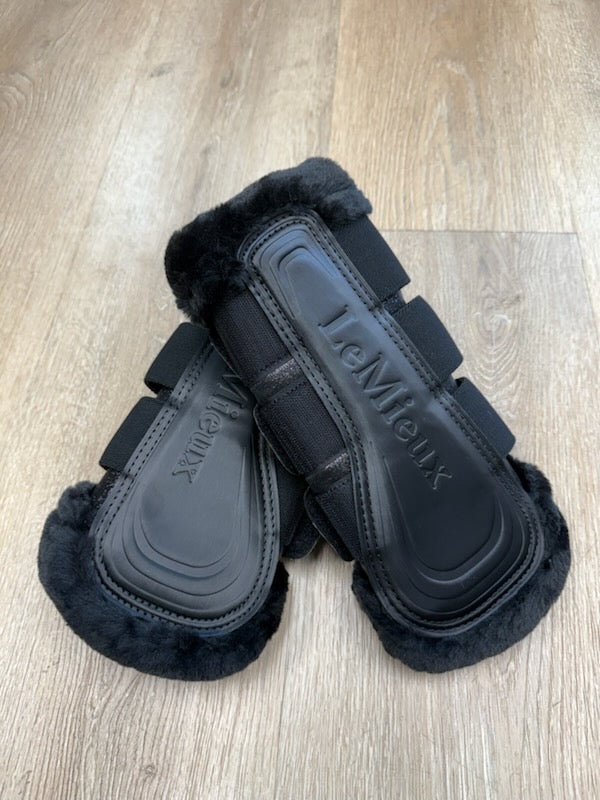 Pair of black equestrian leg wraps with visible brand logo on a wooden floor.