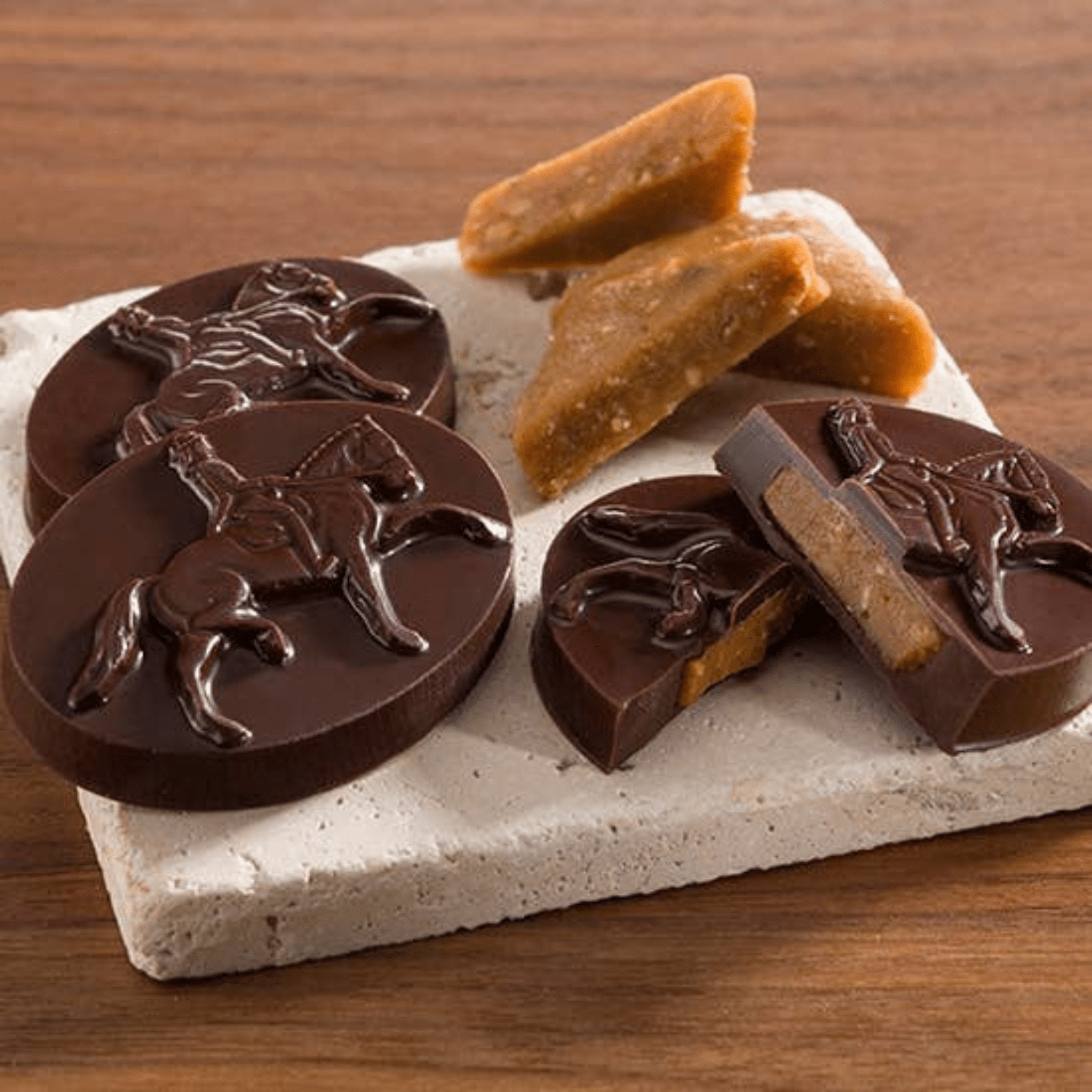 Chocolate candies with horse designs on a stone platter with caramel pieces on a wooden surface