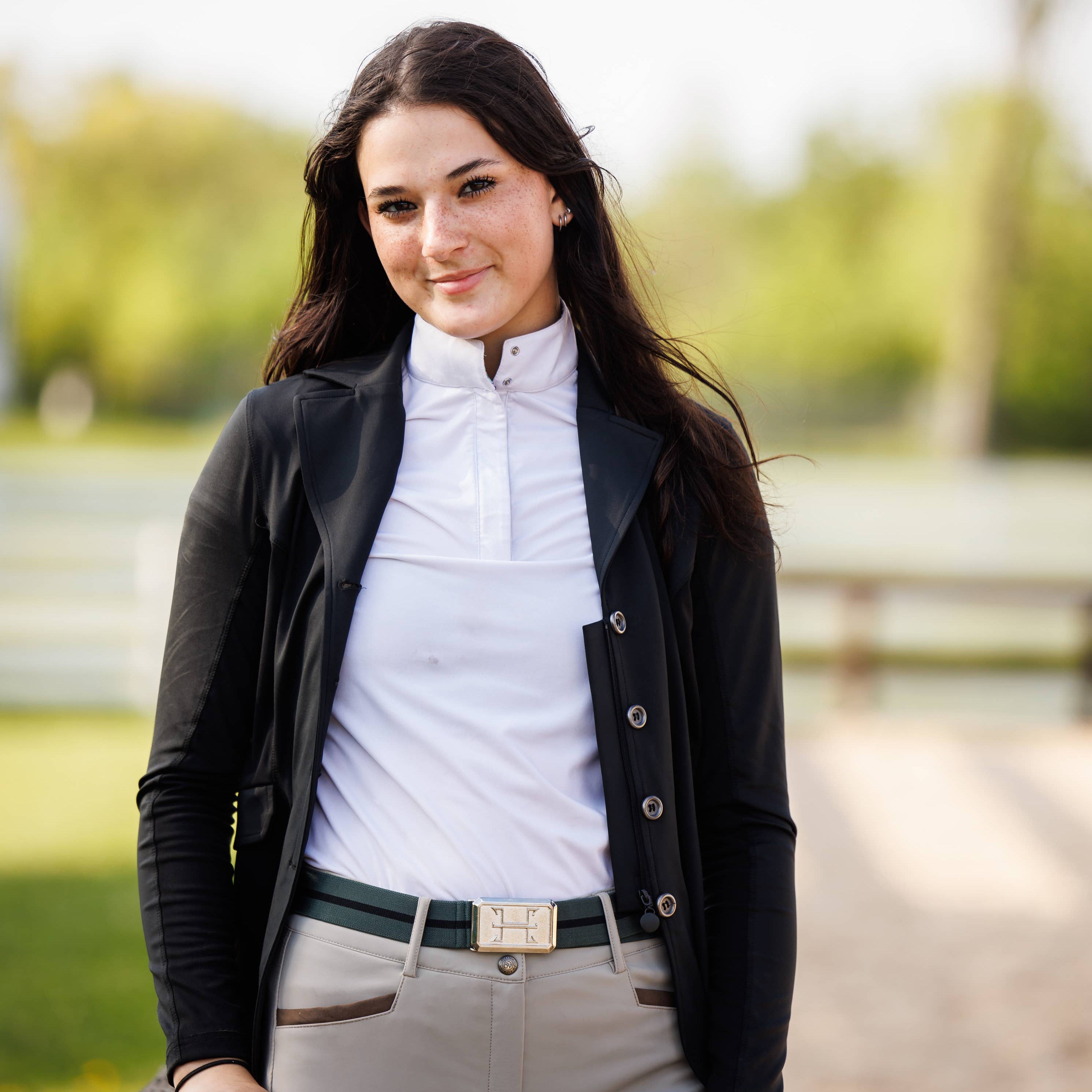Woman in equestrian attire standing outdoors with a blurred background