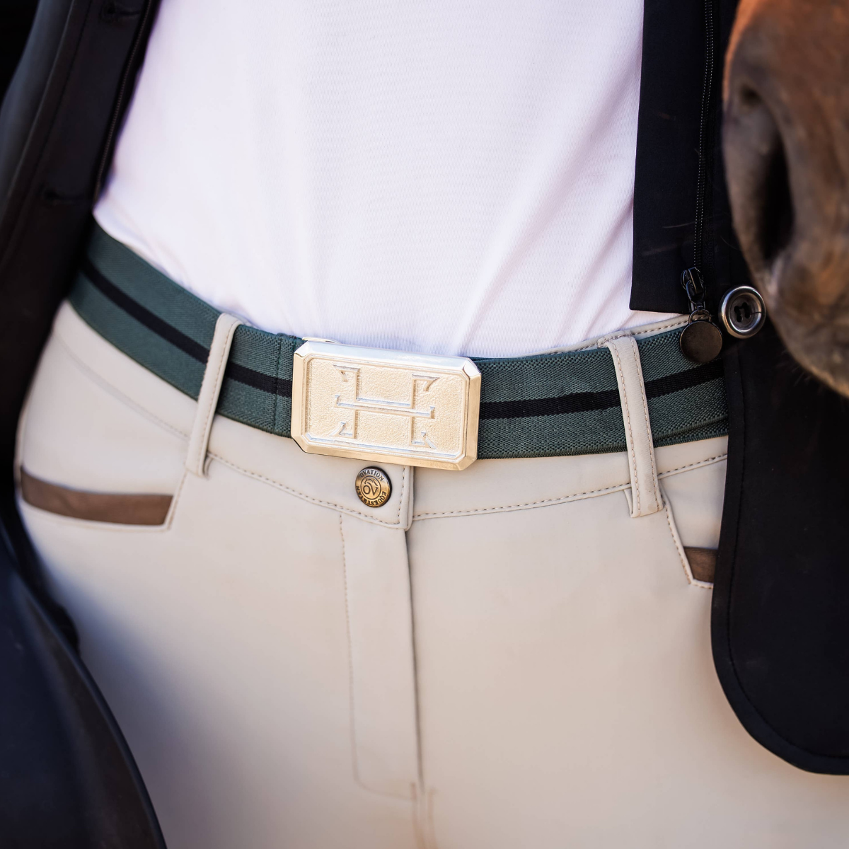 Close-up of a person wearing a green belt with a gold buckle, beige pants, and a white shirt.