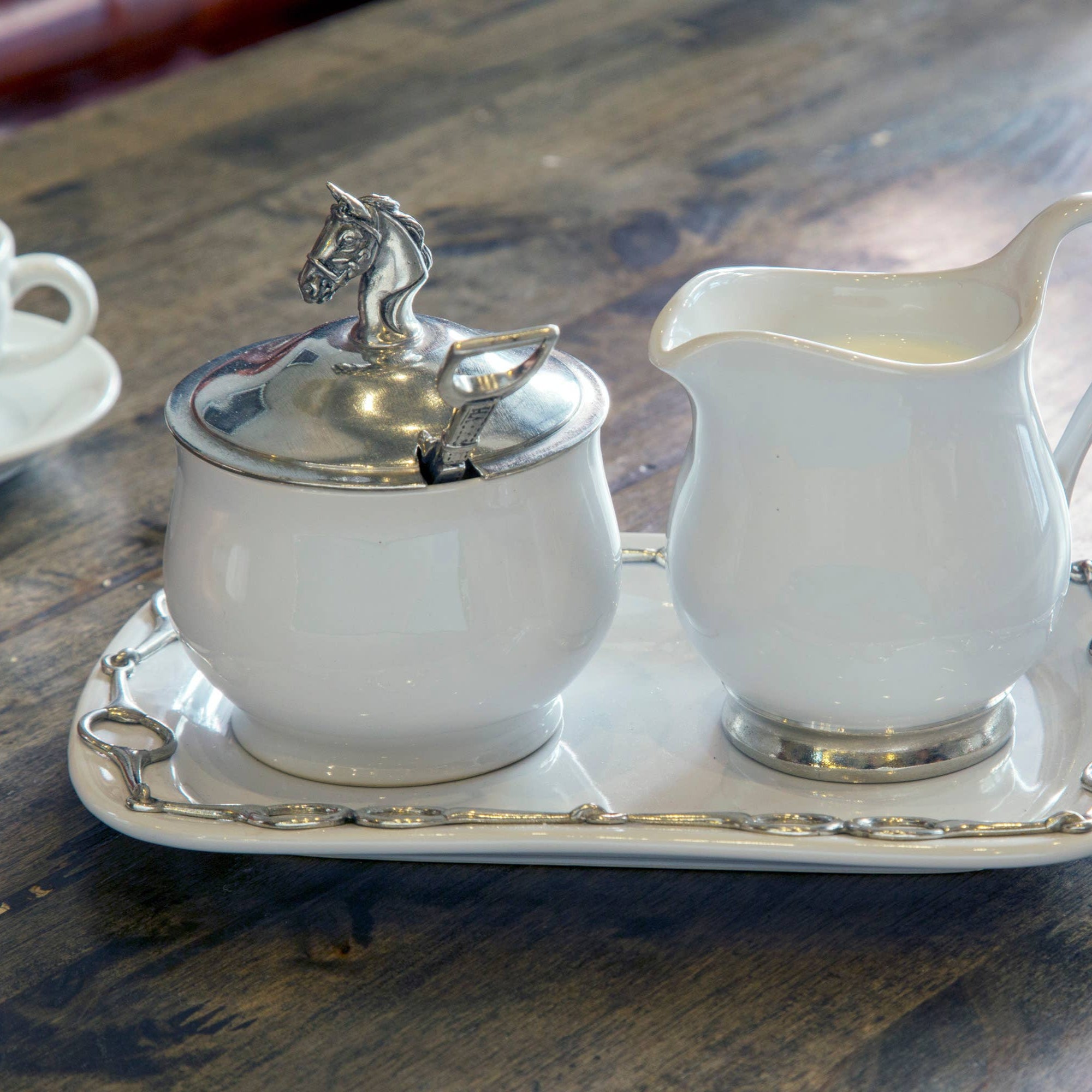 White ceramic sugar bowl and creamer set with silver horse finial on a wooden surface
