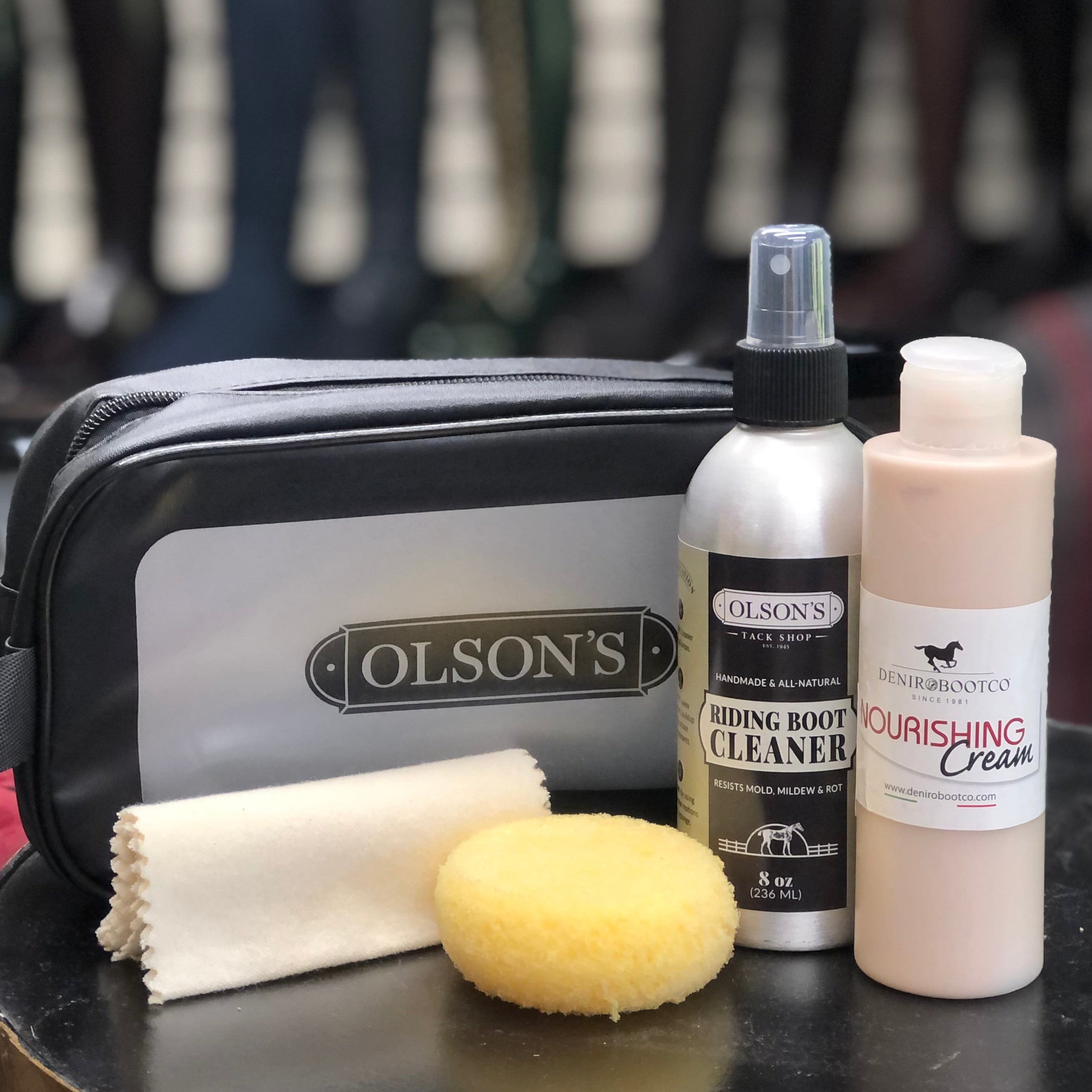 Olson's leather care products including a spray bottle, cream, and sponge on a table with shoes in the background.