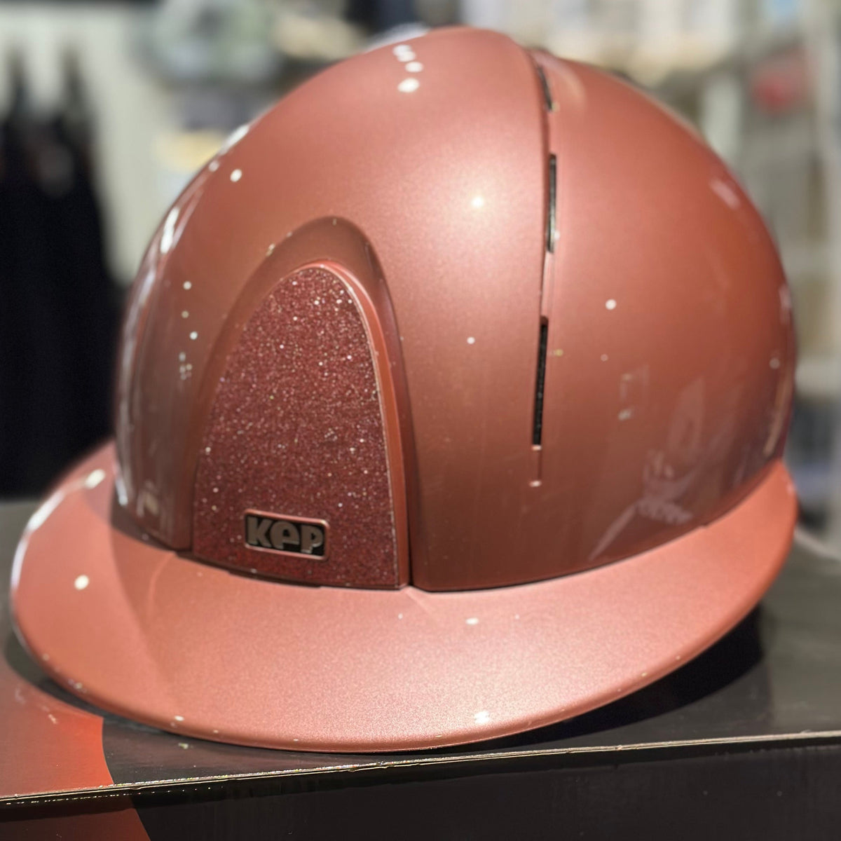 A metallic pink horse riding helmet displayed on a black box inside a store.