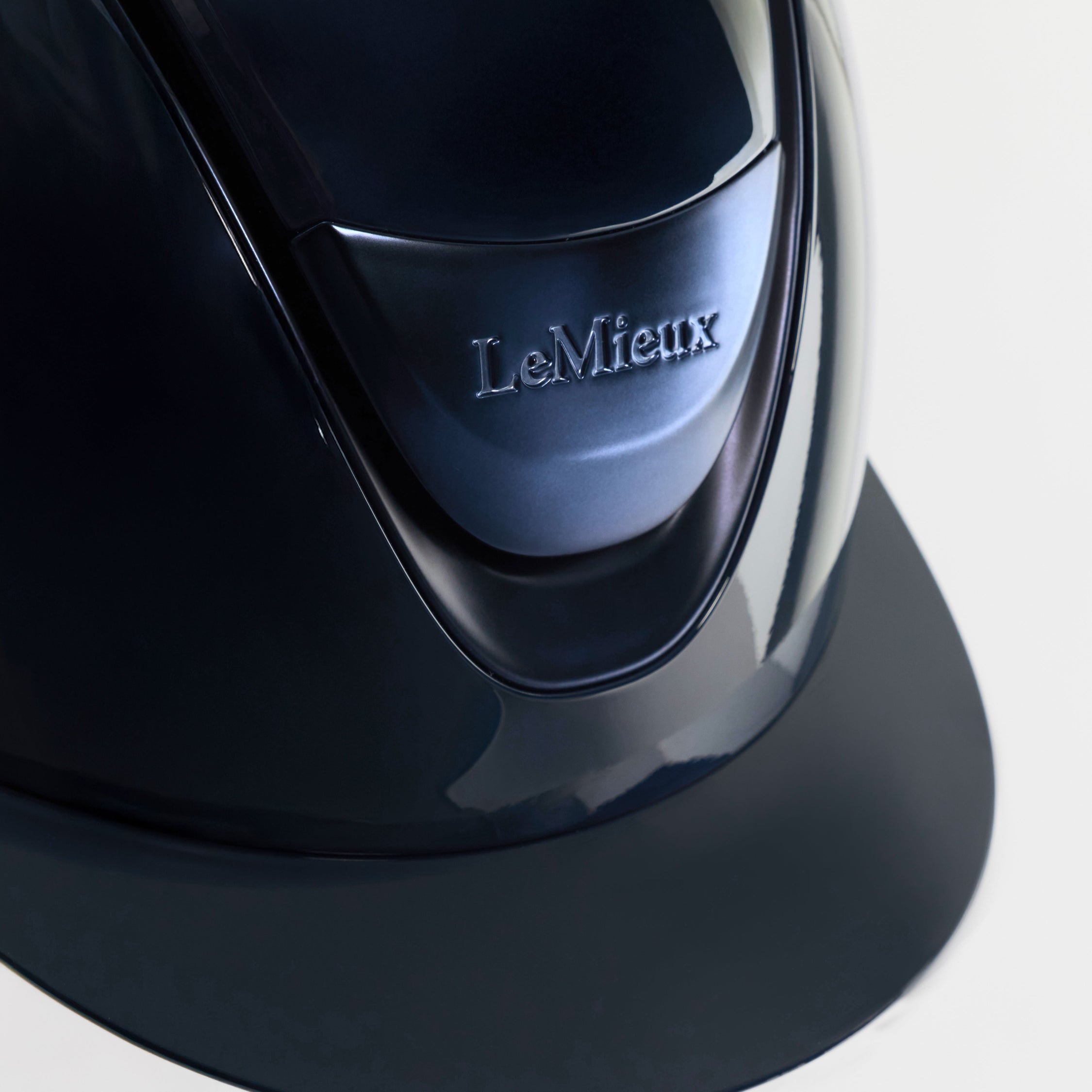 Close-up of a glossy black LeMieux riding helmet showing the front visor and embossed brand logo on a light gray background.
