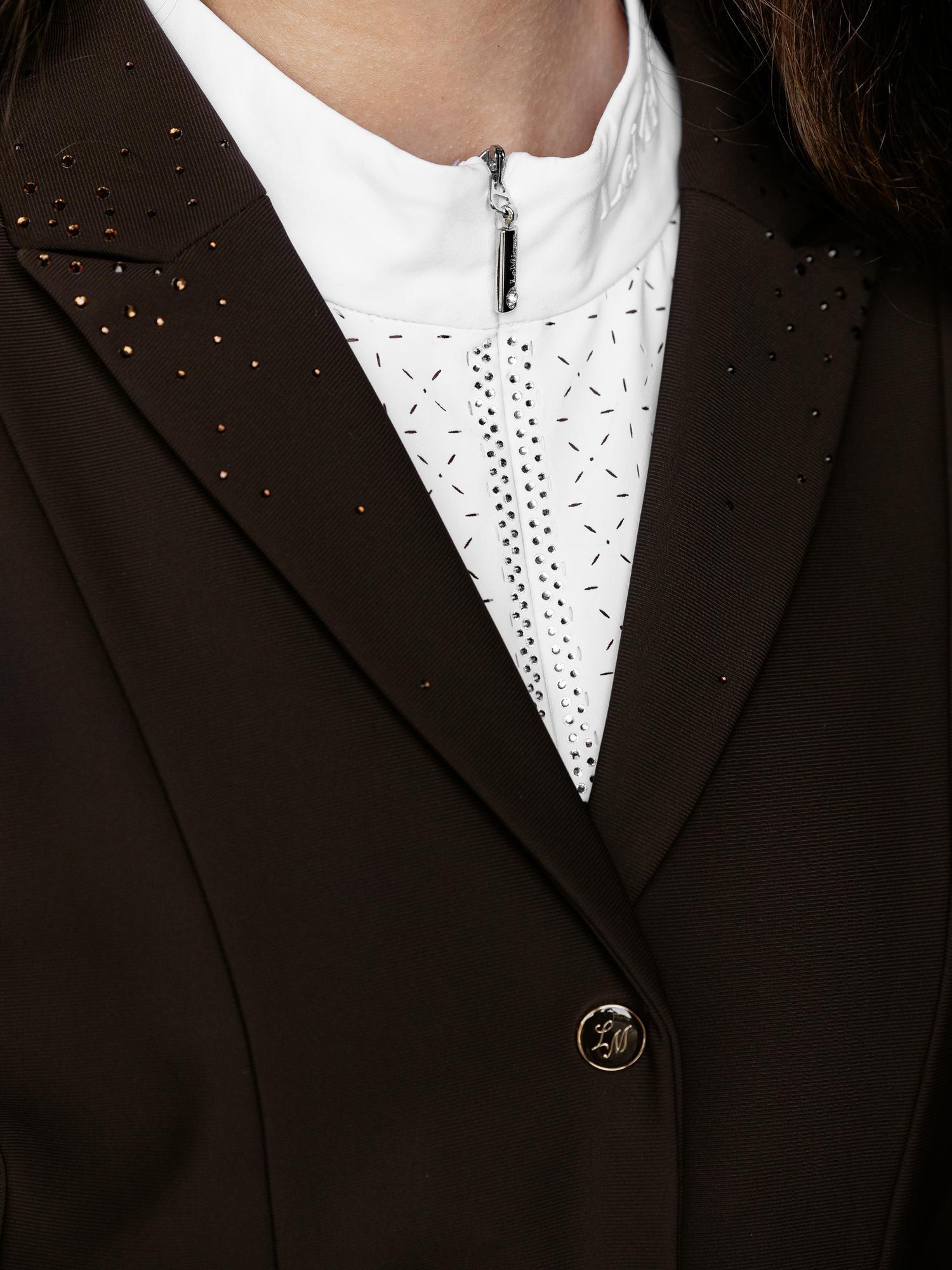 Close-up of a person wearing a brown blazer with a white lace shirt underneath.