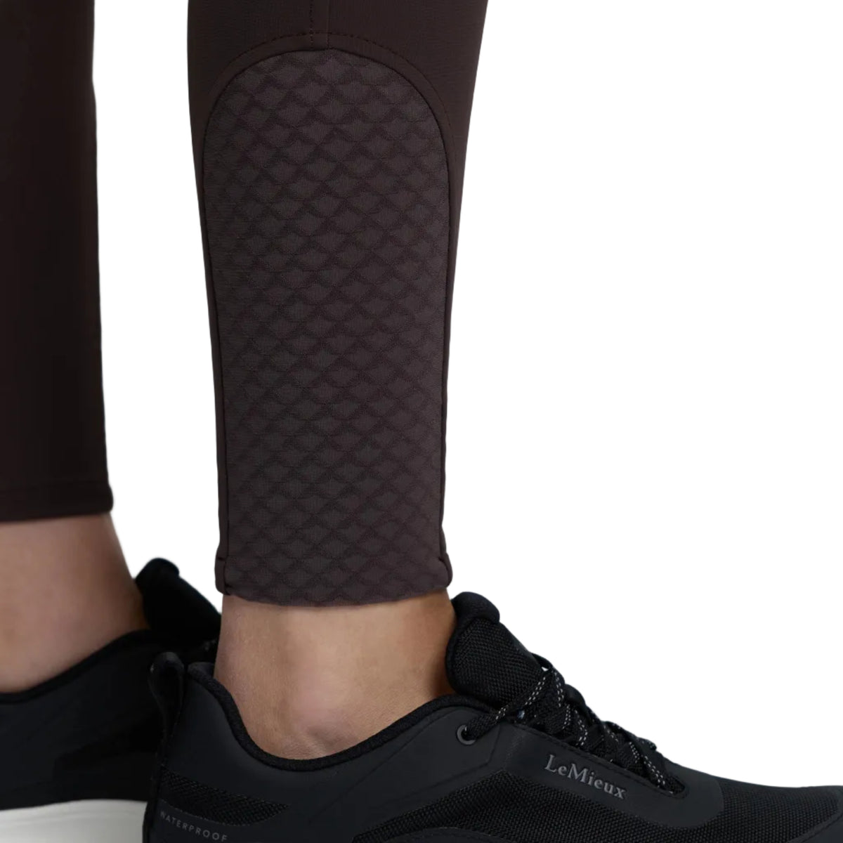 Black LeMieux athletic sneakers with a thick white sole, shown on a model wearing dark brown textured leggings against a light gray studio background.