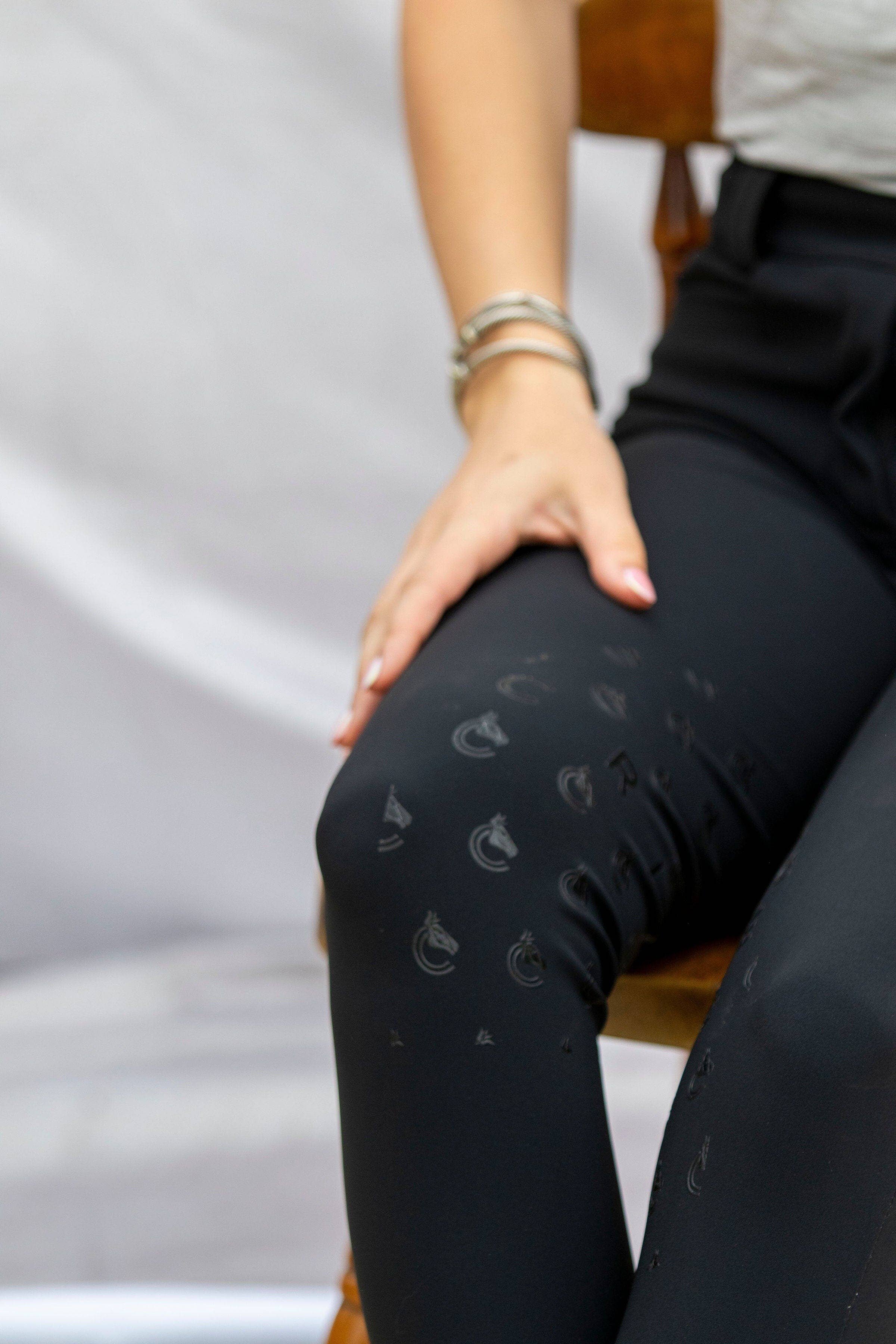Person wearing black leggings with small patterns, sitting on a white surface.