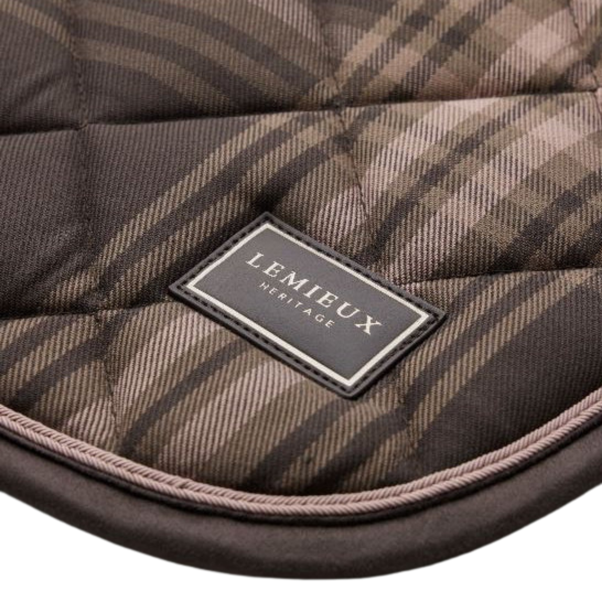 Close-up of a quilted plaid saddle pad with a brown and beige tartan pattern, featuring a black leather patch with the brand name 'LEMIEUX HERITAGE' in gold lettering.