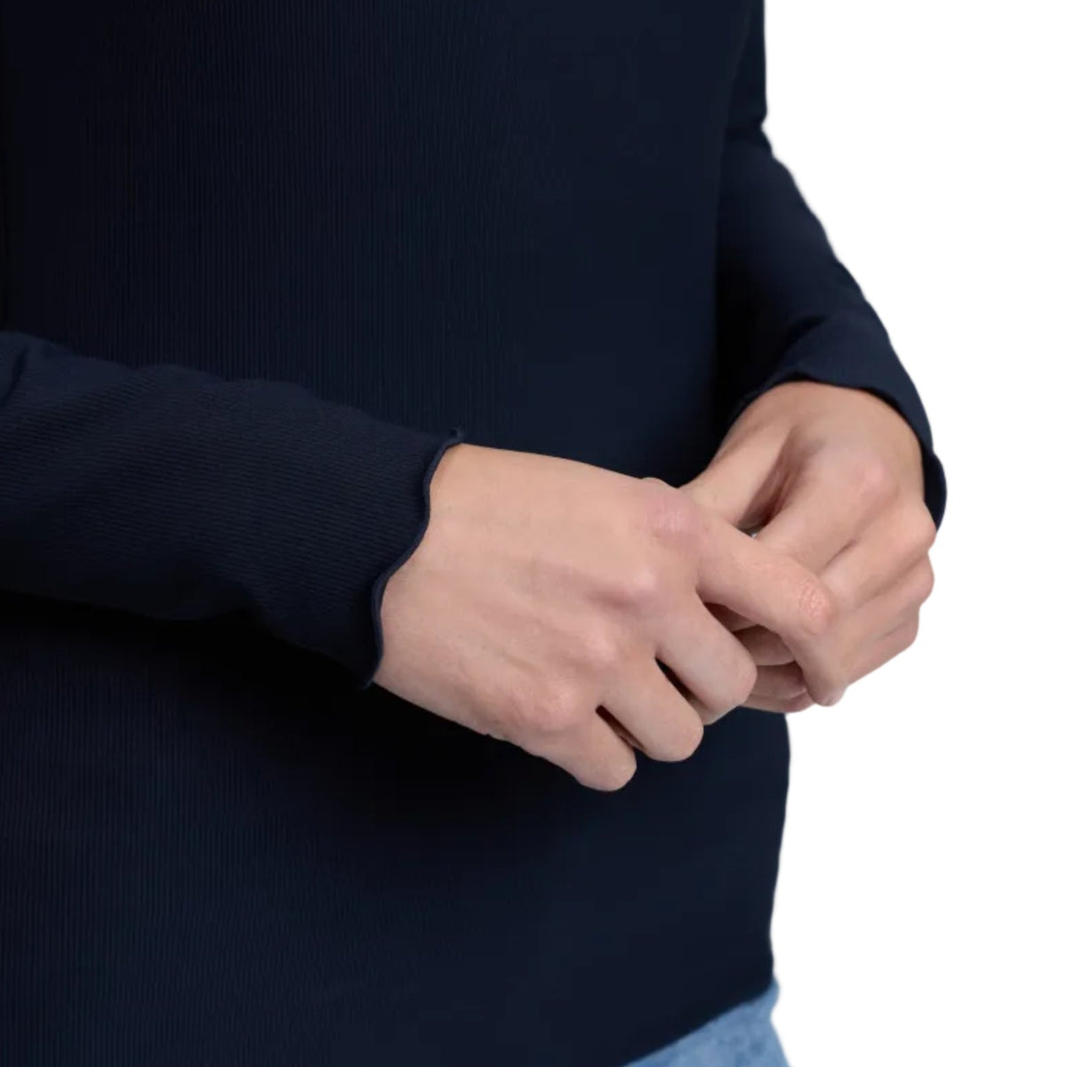 Close-up of a person wearing a dark navy ribbed knit long-sleeve top with light blue jeans, showing the hands adjusting the cuffs.