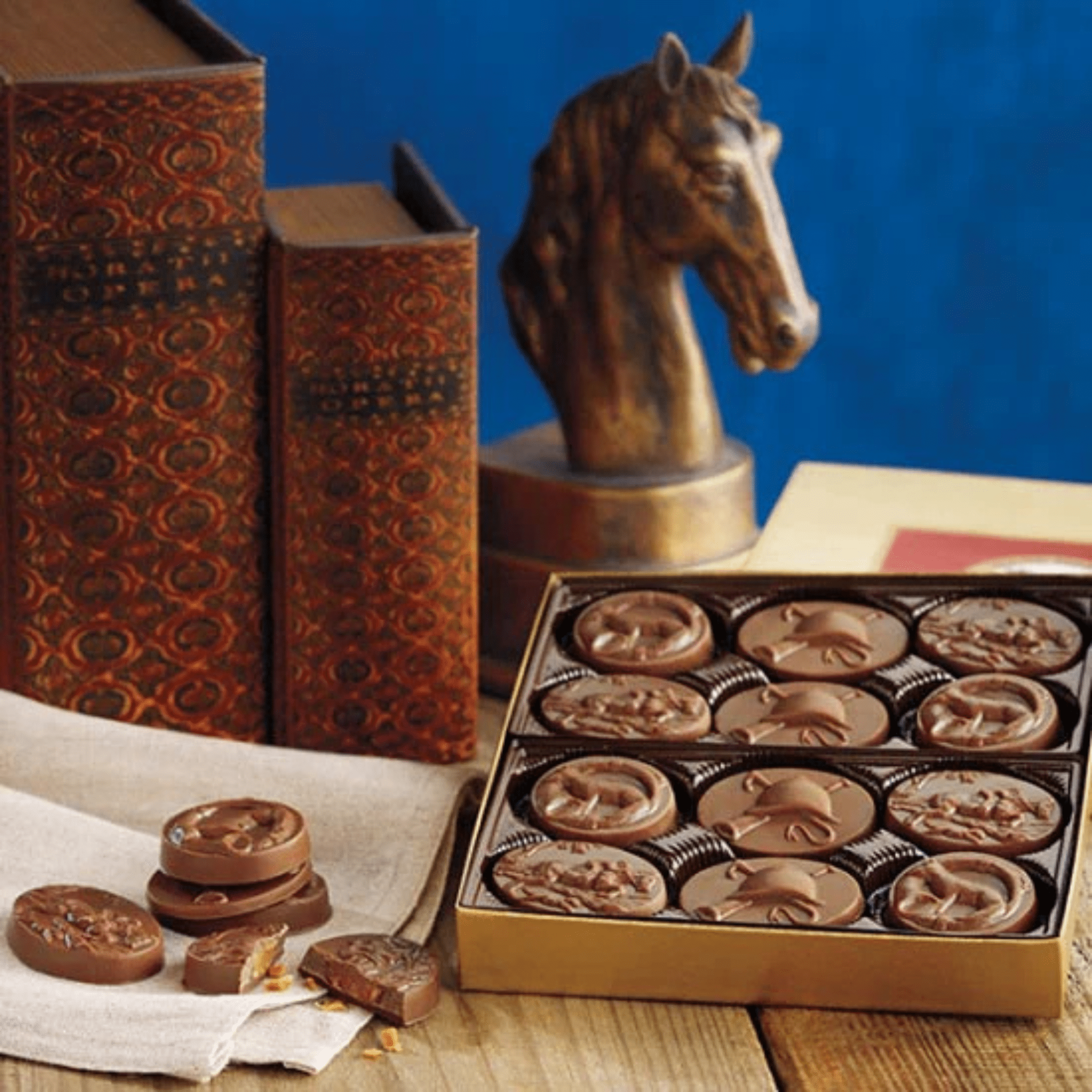 Box of chocolate horse figurines with decorative books and a horse statue on a blue background