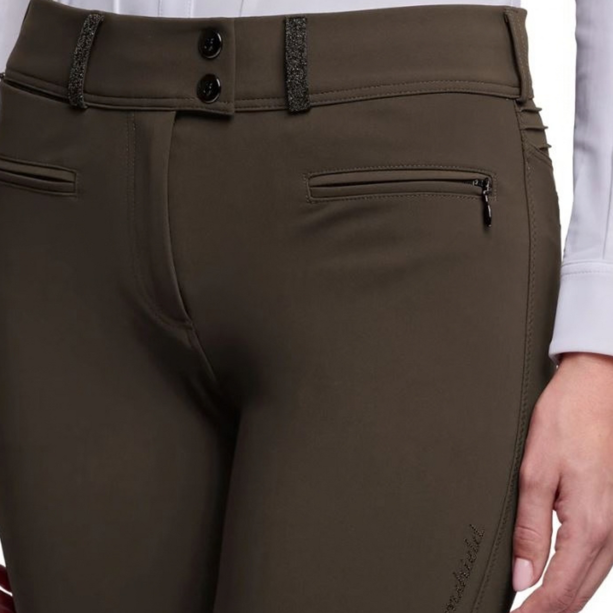 Close-up of a person wearing olive brown equestrian riding pants, showing the back waistband with two black buttons, side zip pocket, and a hand holding the side of the garment.
