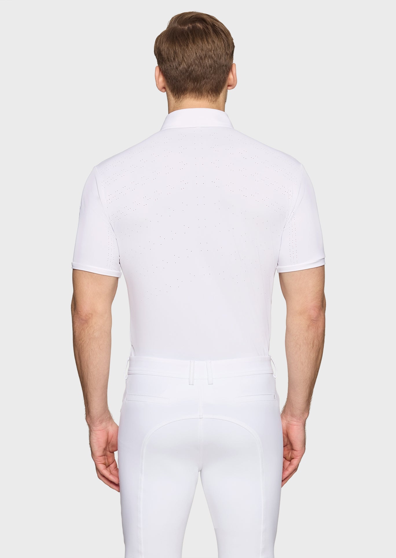 Man wearing a white polo shirt and white pants on a light gray background