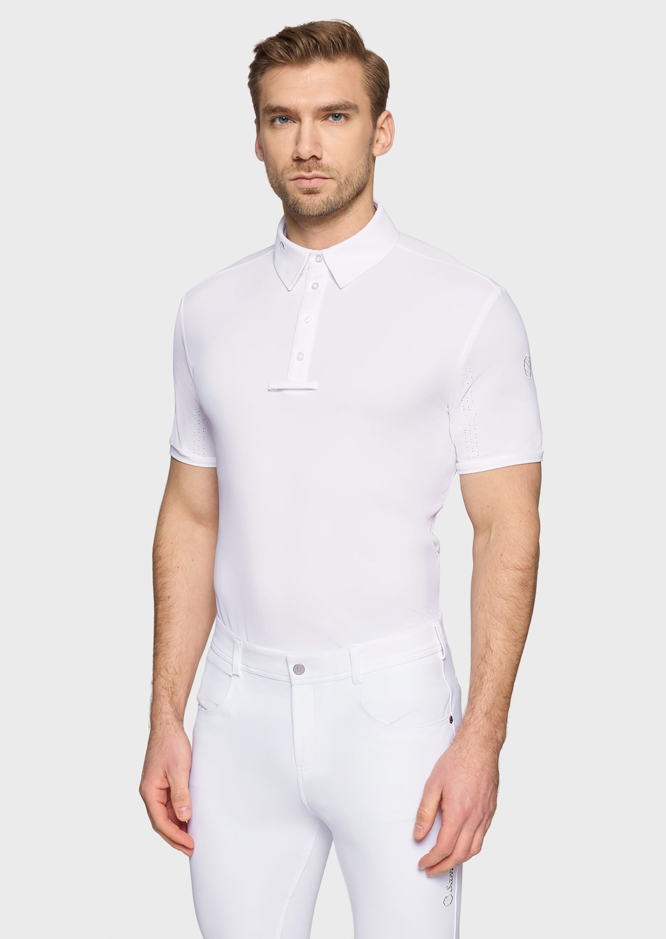 Man wearing a white equestrian jumpsuit on a light gray background