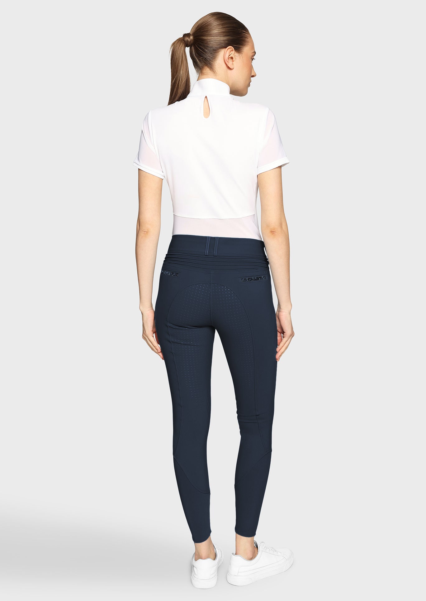 Woman wearing navy riding pants and a white shirt on a white background