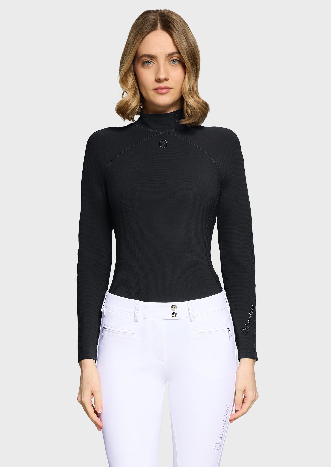 Woman wearing a black turtleneck top and white pants on a light gray background