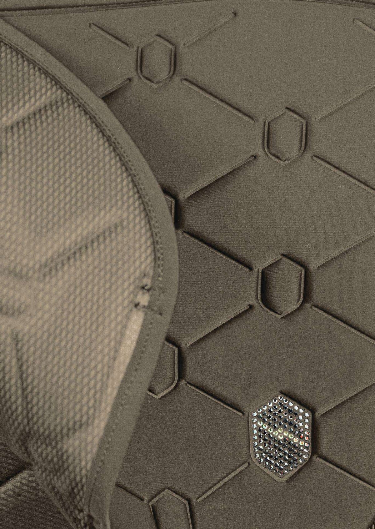 Close-up detail of a dark olive green protective pad or armor plate with a honeycomb pattern, featuring a small hexagonal metallic logo badge.
