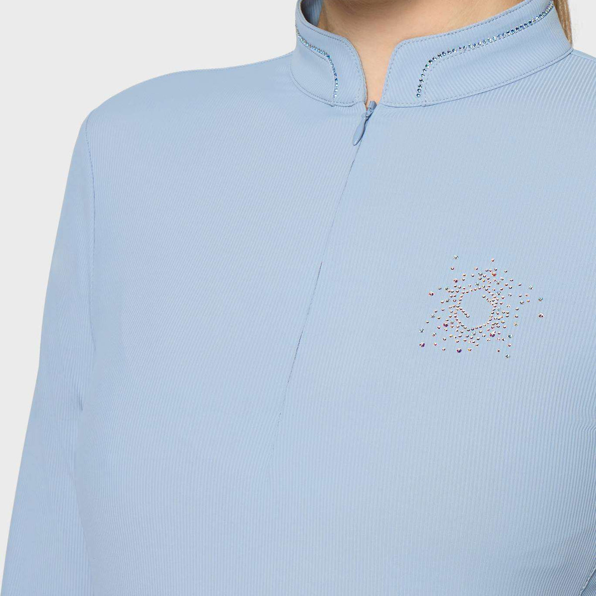 A close-up of a model wearing a light blue ribbed long-sleeve top with a mock neck and a small multicolor rhinestone graphic on the left chest, set against a plain light gray background.