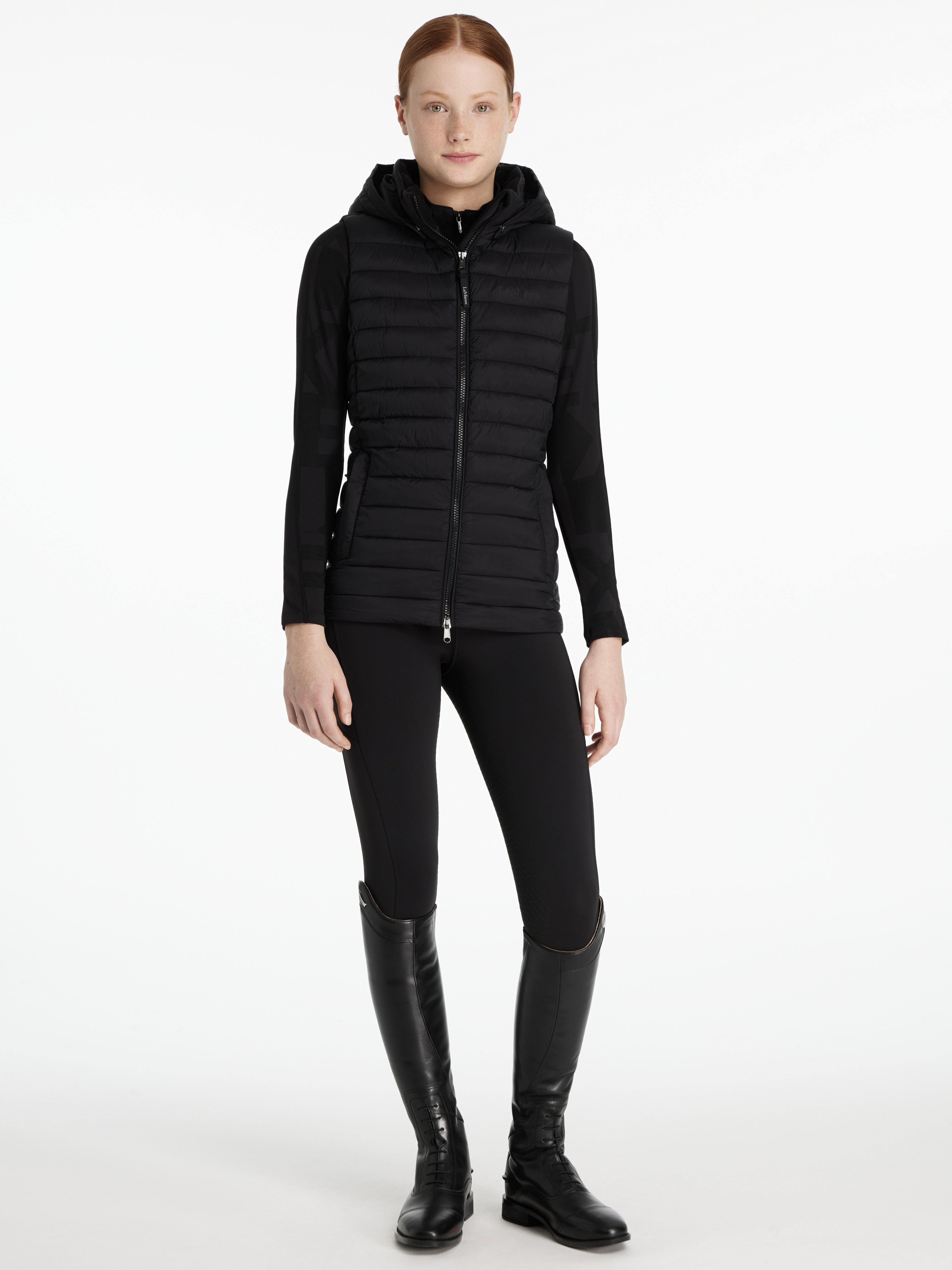 Woman wearing a black quilted jacket, black leggings, and black boots on a white background