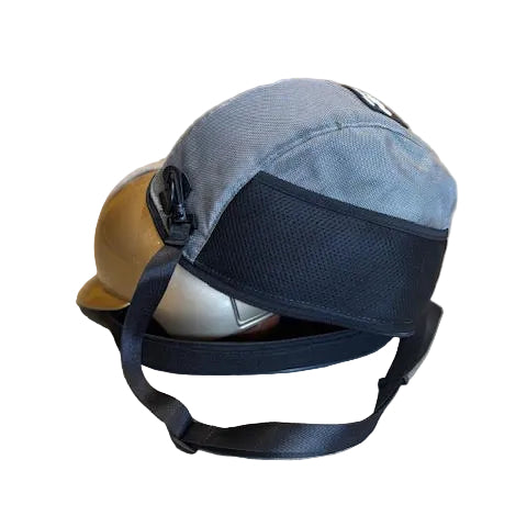 A gray and black trucker-style cap with a chin strap, resting on a beige floor in a blurred indoor setting.