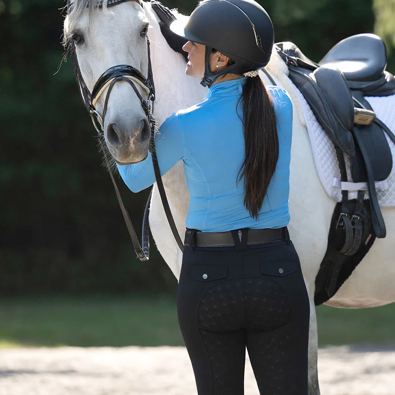 Woman in equestrian attire standing next to a white horse in an outdoor setting