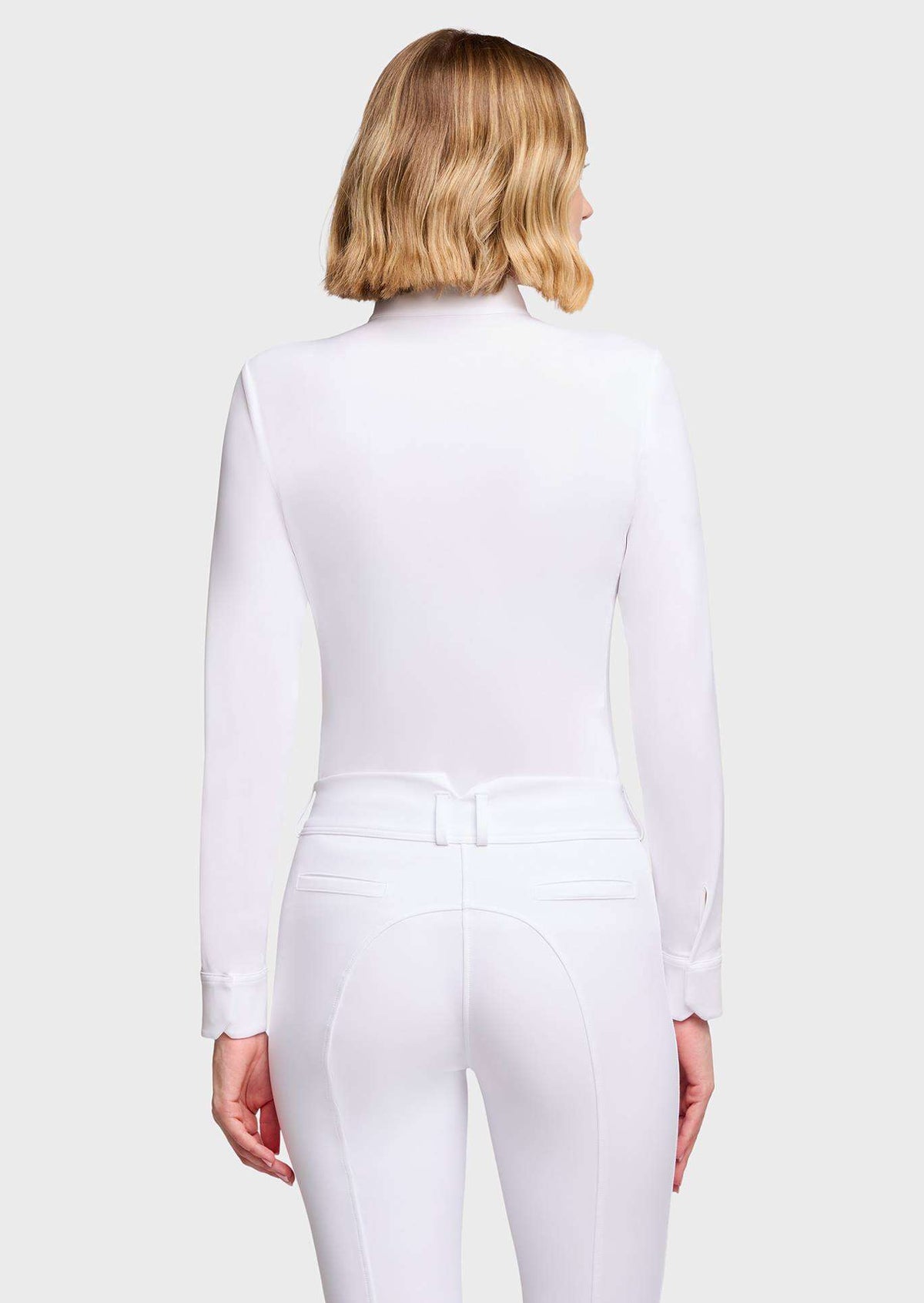 A woman shown from the back wearing a fitted white long-sleeve top and matching white riding-style pants against a light gray studio background.