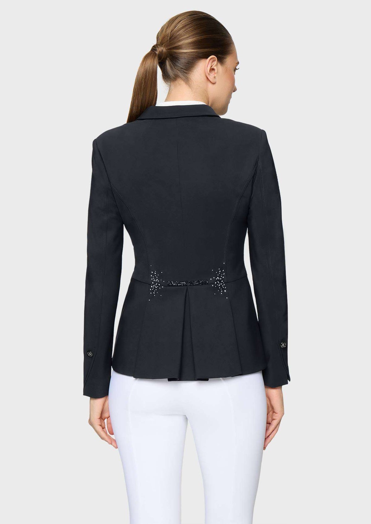 A woman shown from the back wearing a structured black blazer with a peplum-like waist and small embellished detail at the center, paired with white pants, against a light gray studio background.