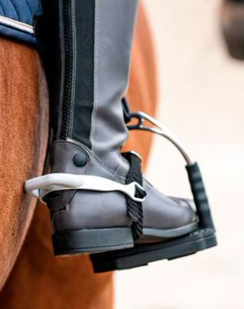 Close-up of a gray equestrian boot with a black strap and silver metal stirrup hardware attached to a horse's footrest.