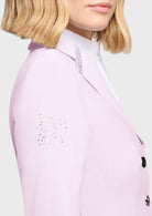 A close-up of a model wearing a light pink blazer with silver rhinestone embellishments on the lapel and sleeve, paired with a white high-neck top.
