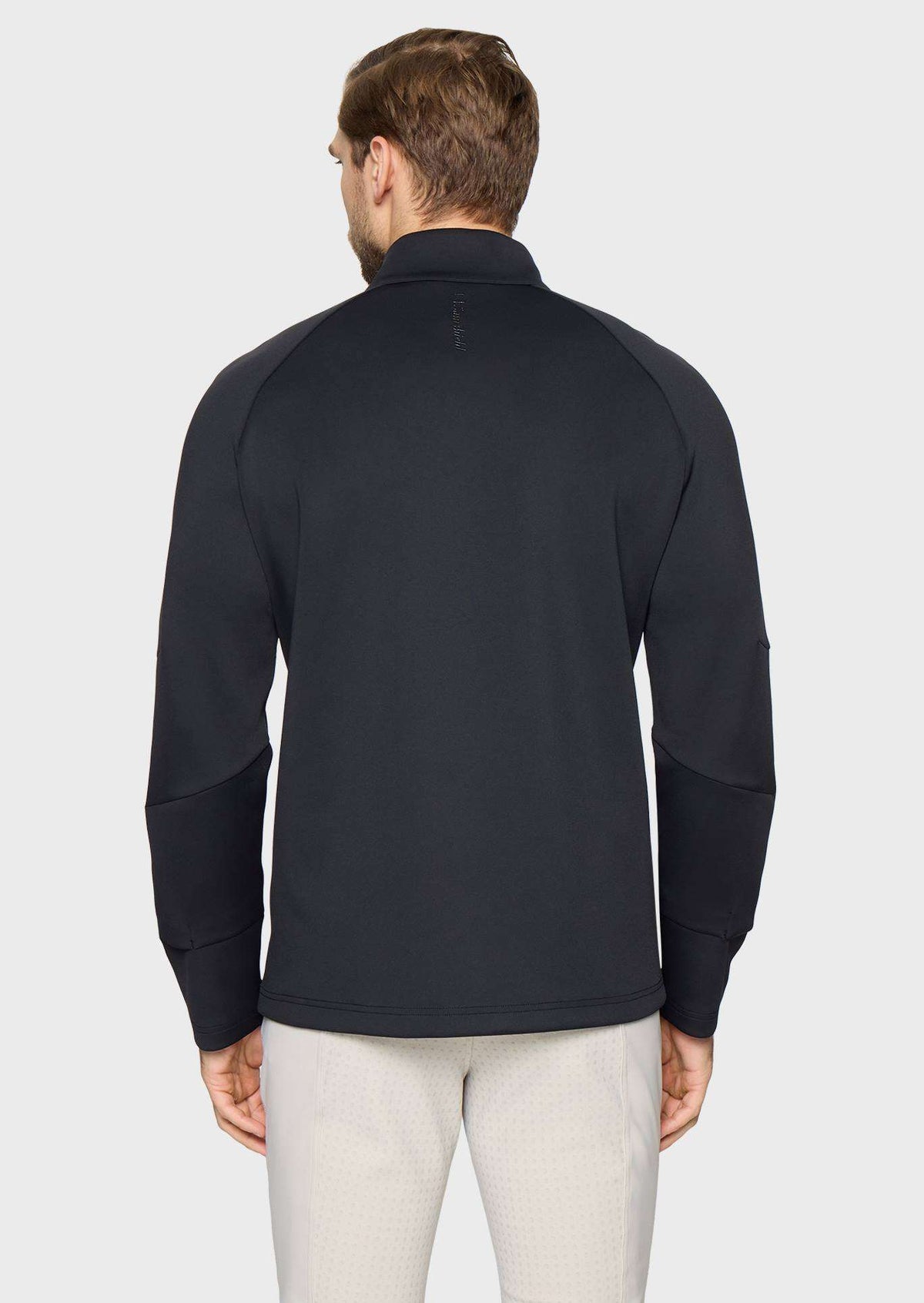 A man viewed from the back wearing a dark navy long-sleeve quarter-zip pullover with contrast knit sleeves, paired with light beige trousers, against a light gray studio background.