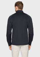 A man viewed from the back wearing a dark navy long-sleeve quarter-zip pullover with contrast knit sleeves, paired with light beige trousers, against a light gray studio background.