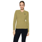 A woman modeling a ribbed cable-knit V-neck sweater in olive green, paired with dark navy pants, against a light gray studio background.