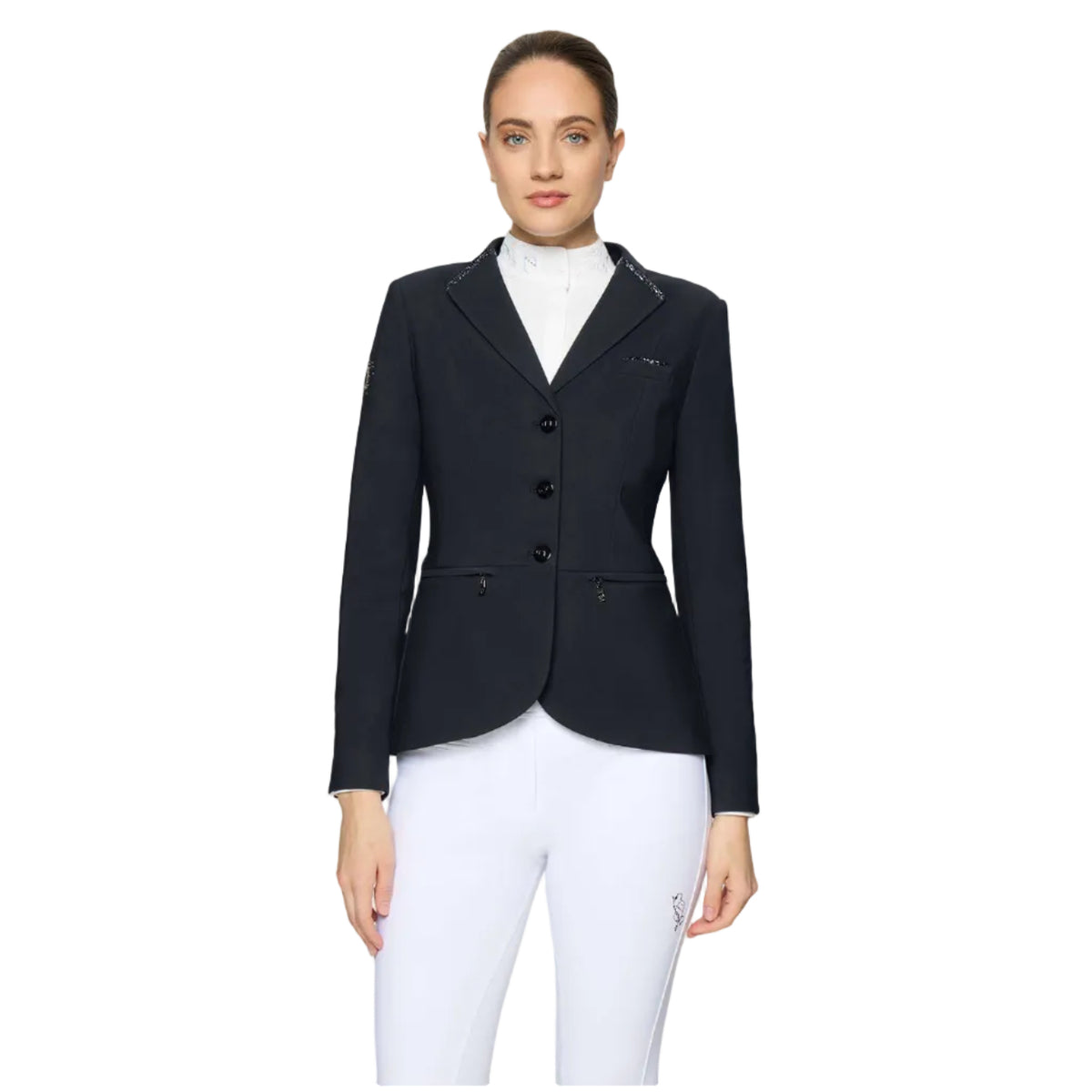 A woman modeling a black equestrian-style blazer with three front buttons, notched lapels, and flap pockets, worn over a white high-neck top and white riding breeches, against a light gray studio background.