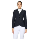 A woman modeling a black equestrian-style blazer with three front buttons, notched lapels, and flap pockets, worn over a white high-neck top and white riding breeches, against a light gray studio background.