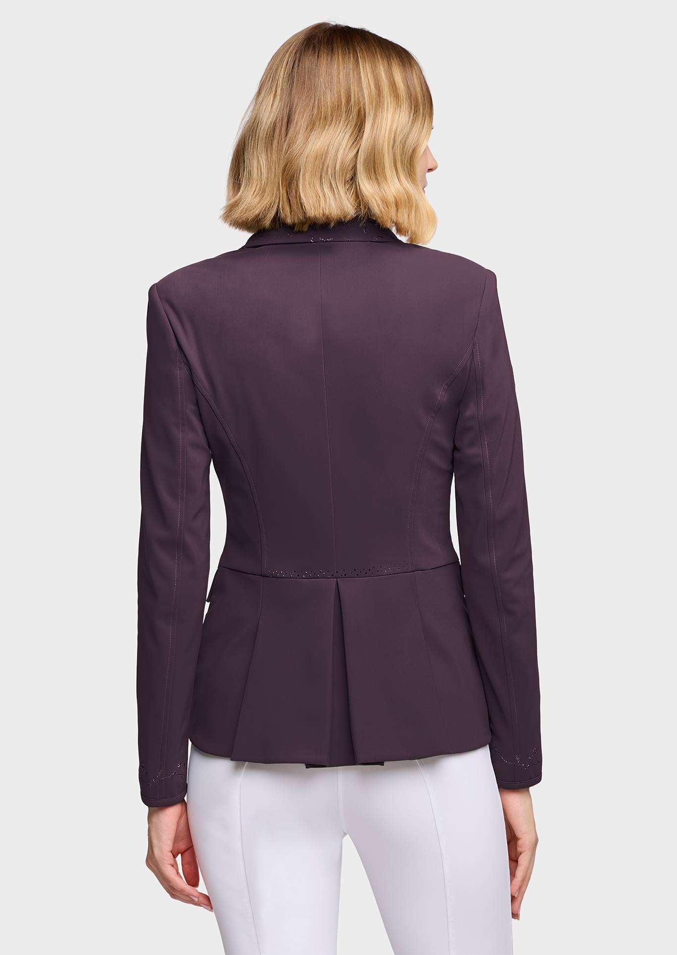 A woman viewed from the back wearing a dark plum purple structured blazer with a peplum waist and white pants, set against a solid light gray background.