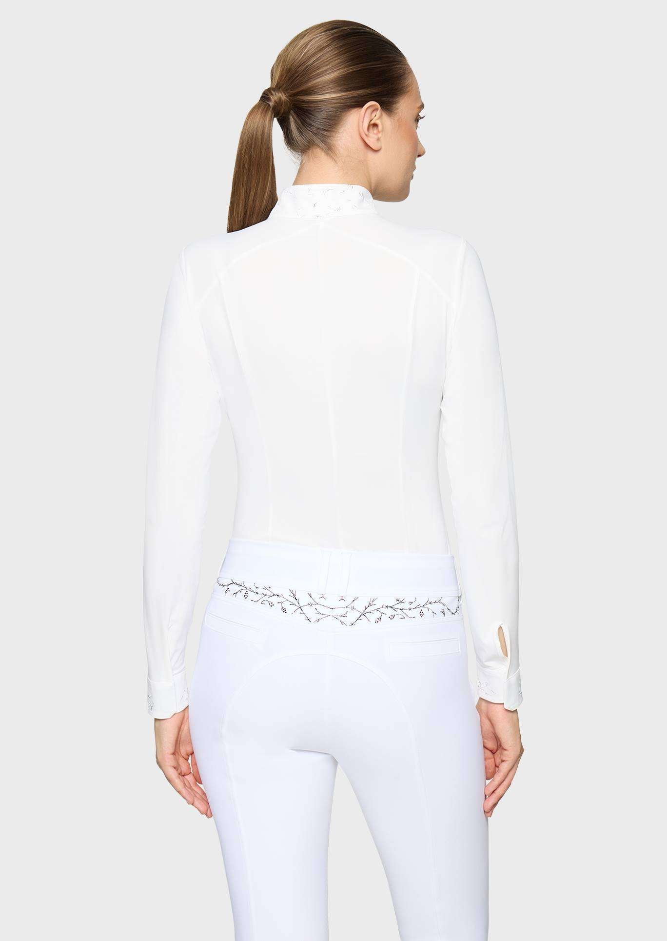 A woman shown from the back wearing a white long-sleeve mock-neck equestrian-style top and matching white fitted pants with a decorative silver embroidered waistband.