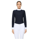 A woman modeling a fitted long-sleeve equestrian-style top in dark navy with a contrasting white mock neck and white cuffs, paired with white riding pants, against a light gray studio background.