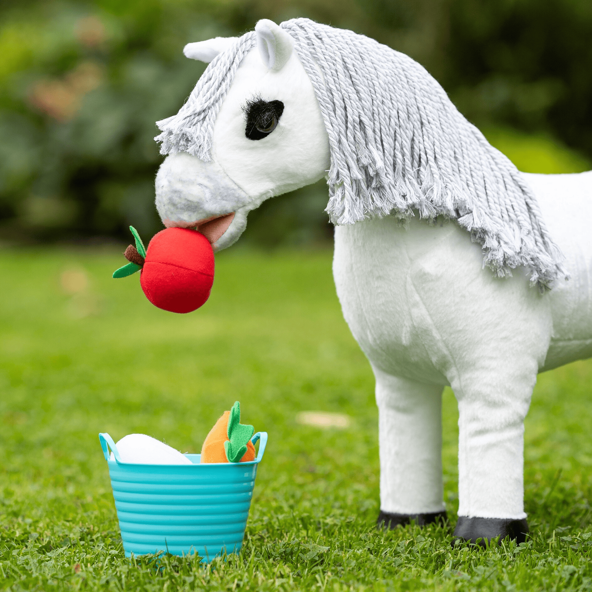 White plush horse toy with a red apple and small basket on grass