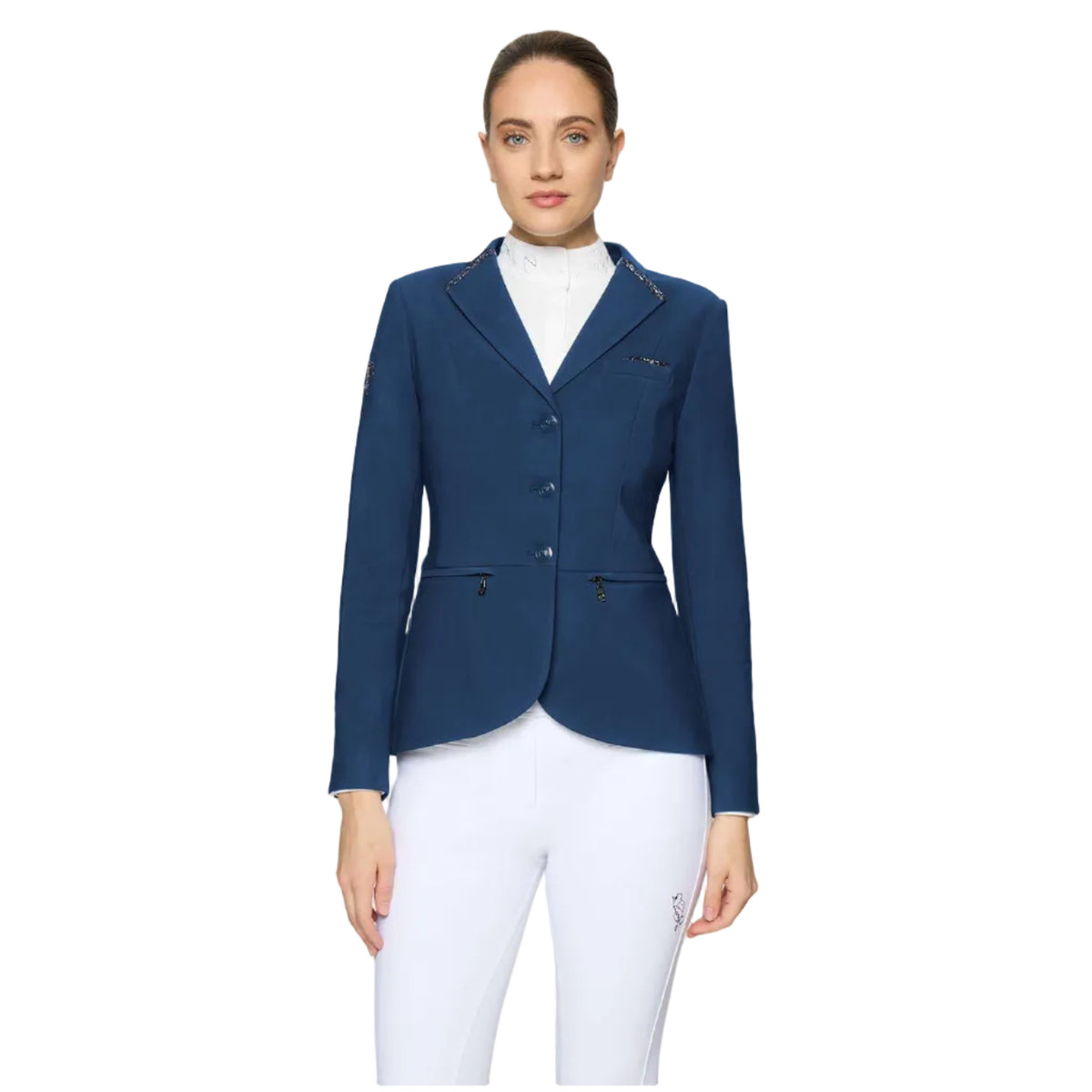 A woman modeling a navy blue equestrian blazer over a white high-collar shirt and white riding breeches, shot against a light gray studio background.