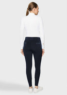 A woman shown from the back wearing a white mock-neck long-sleeve top and dark navy blue skinny pants, paired with white sneakers, against a light gray studio background.