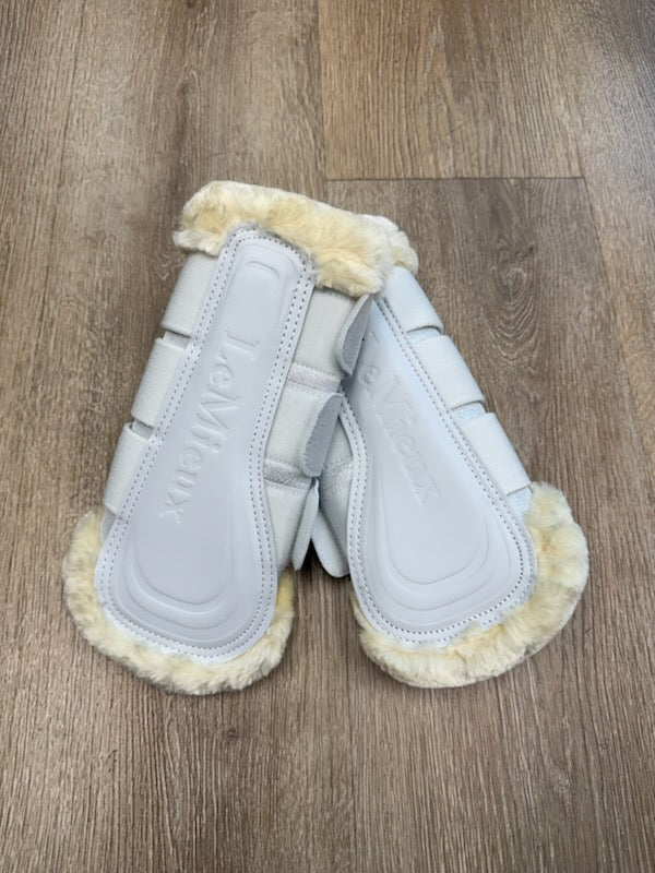 Pair of white leather mittens with fur trim on a wooden floor.