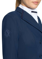 Close-up of a navy blue equestrian jacket with decorative silver rhinestone embroidery on the sleeve and lapel, worn by a model over a white high-collar shirt.