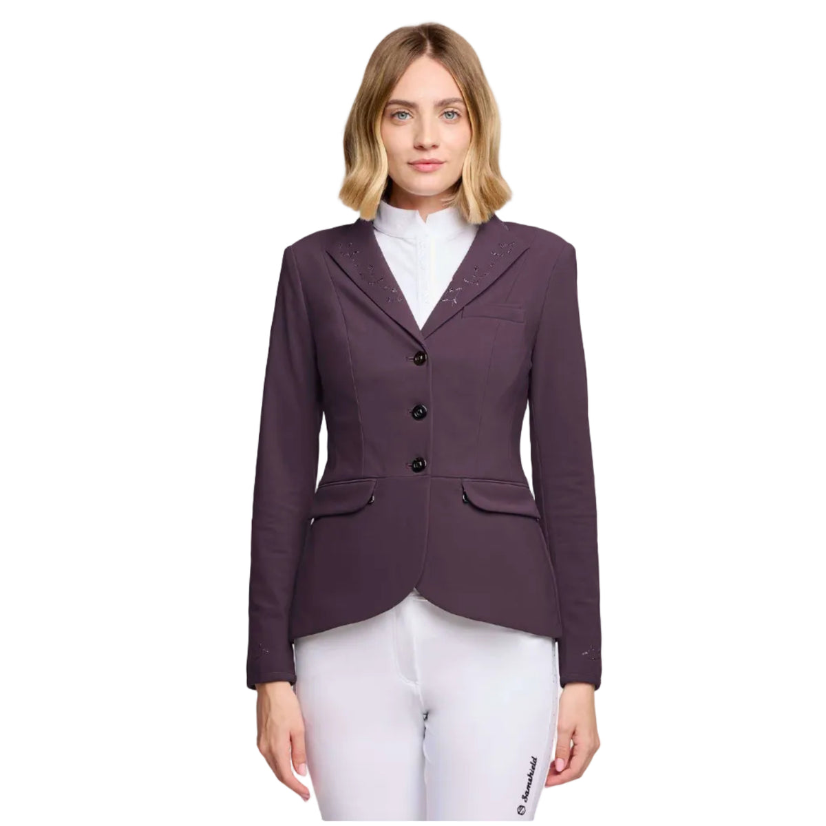 A woman modeling a dark plum purple equestrian blazer with three-quarter lapels, black buttons, and subtle embroidered detailing on the chest, paired with white riding breeches and a white collar shirt, against a light gray studio background.
