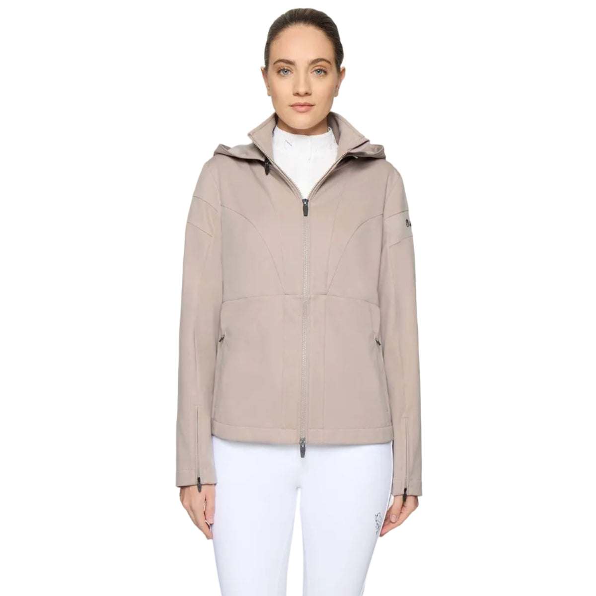 A woman modeling a light taupe hooded jacket with a full front zipper, zippered hand pockets, and zip cuffs, worn over a white turtleneck and white pants, against a light gray studio background.