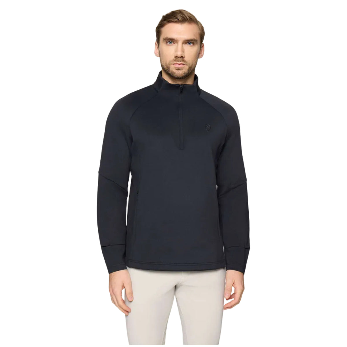 A man wearing a dark navy long-sleeve quarter-zip pullover with a small embroidered logo on the left chest, paired with light beige pants, against a solid light gray background.