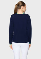 A woman viewed from the back wearing a navy blue knit sweater with light green trim at the crew neck and cuffs, paired with white pants, against a light gray studio background.