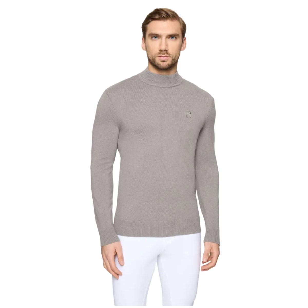 A man wearing a light gray mock neck knit sweater with a small embroidered logo on the chest, paired with white pants, against a light gray background.
