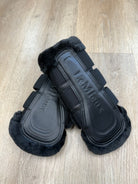 Pair of black equestrian leg wraps with visible brand logo on a wooden floor.