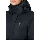 Close-up of a person wearing a black hooded puffer jacket with a small shield-shaped embroidered logo patch on the left chest, photographed against a light gray studio background.