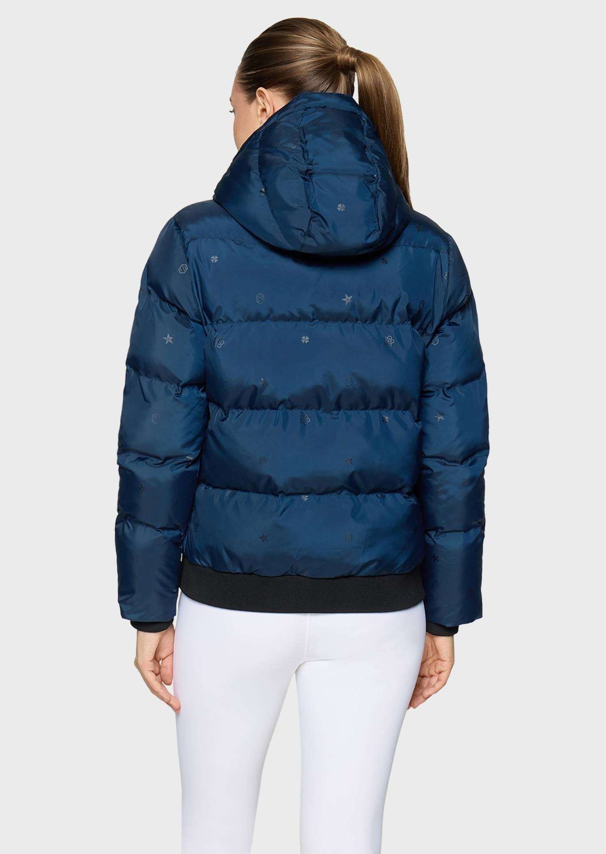 A woman viewed from the back wearing a navy blue puffer jacket with a small star pattern and a black ribbed hem, paired with white leggings, against a plain white background.
